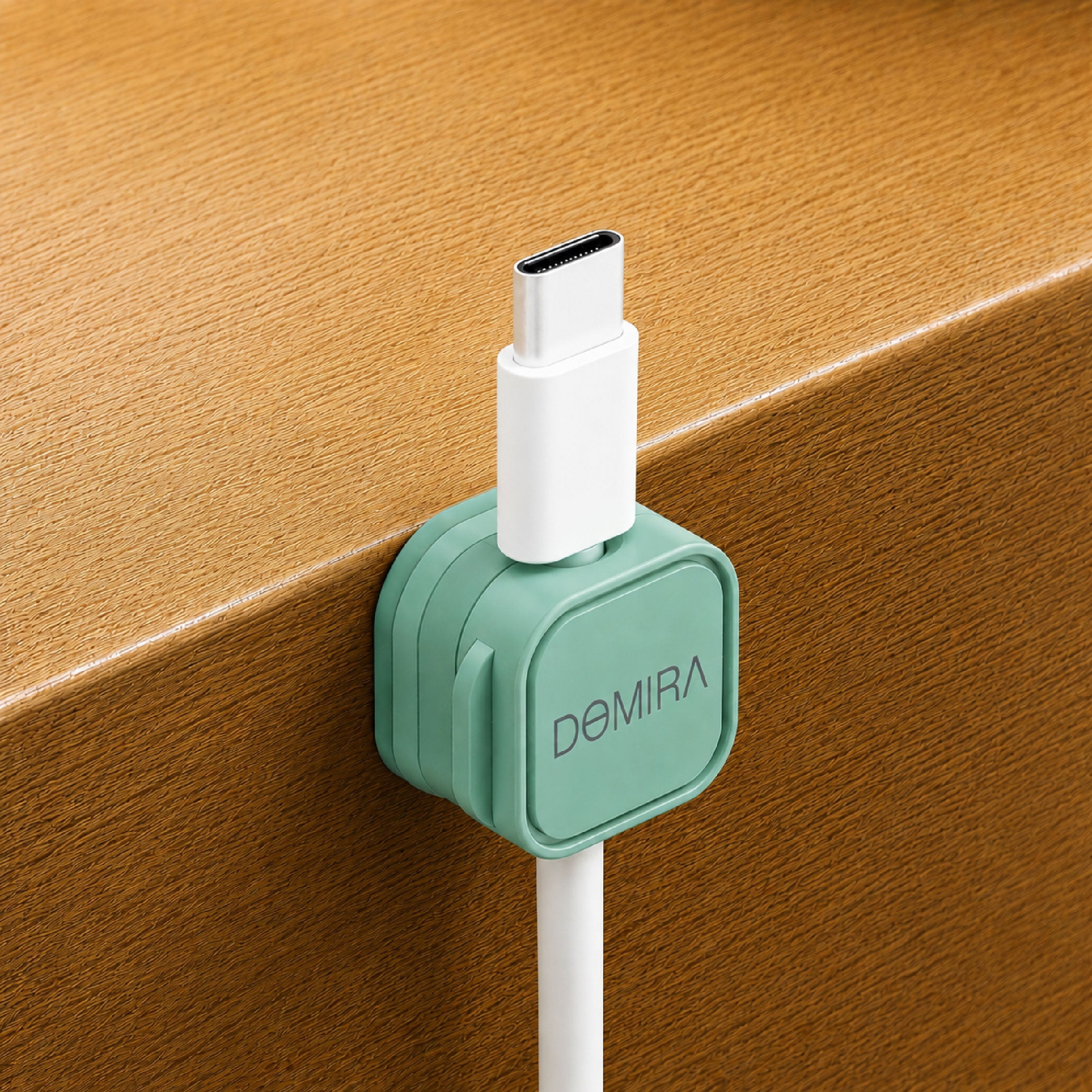 Green magnetic cable clip mounted on the edge of a desk holding a charging cable for easy access and cable organisation.