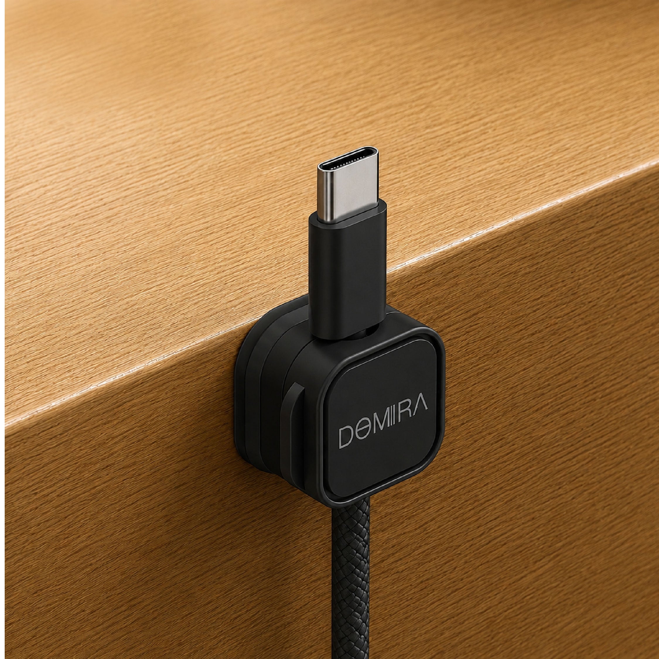 Black magnetic cable clip mounted on the edge of a desk holding a charging cable for easy access and cable organisation.